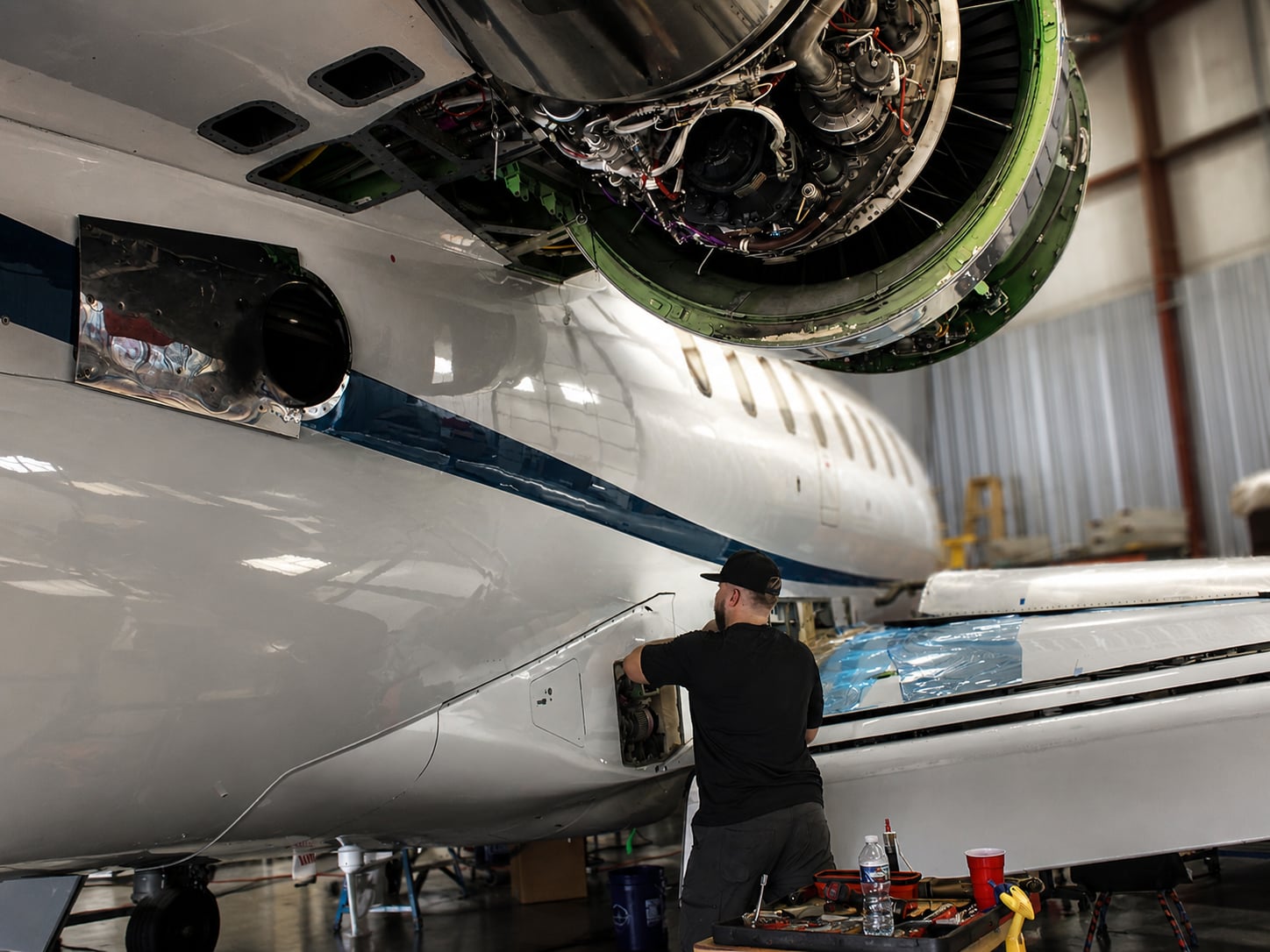 Plane Place Aviation technician performing maintenance beneath an open engine cowling